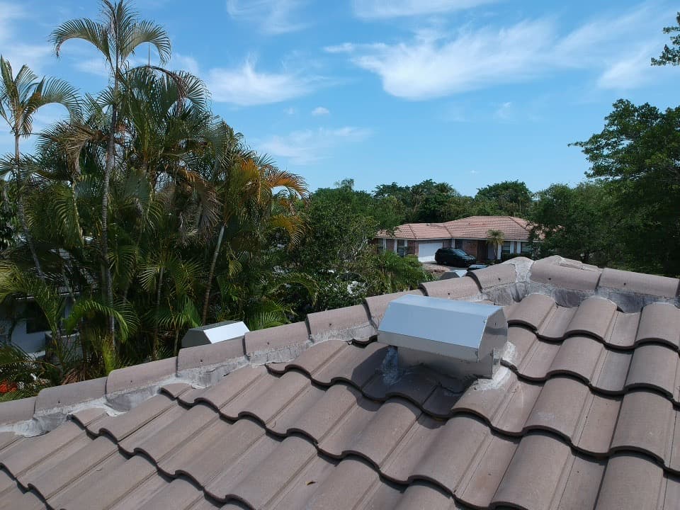 Brown tile roof with a metal vent, palm trees, and a clear blue sky.